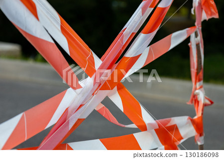 Bright warning tape in orange and white creates a barrier around a construction site in the city during daylight hours, signaling caution Bright warning tape in orange and white creates a barrier around a construction site in the city during daylight hours, signaling caution 130186098