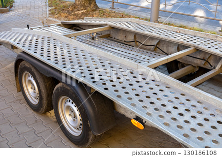 Galvanized trailer sits on asphalt beside a tree, showcasing a sturdy design with multiple holes for drainage and weight reduction 130186108