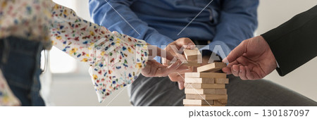 Wide view image of three business people making a tower of wooden pegs 130187097