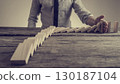 Businessman preventing dominoes from crumbling with palm 130187104