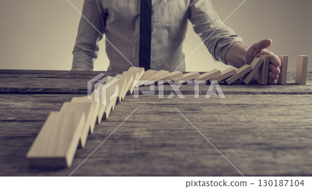 Businessman preventing dominoes from crumbling with palm Businessman preventing dominoes from crumbling with palm 130187104