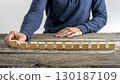 Front view of a man placing 12 blank wooden cubes in a row 130187109