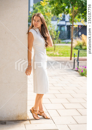 Young woman wearing a white midi dress walking outdoors in Old Money style. Concept of timeless fashion, graceful femininity and understated elegance in modern lifestyle. 130187756