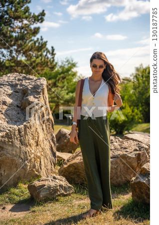Young woman dressed in white vest and green trousers posing outdoors in Old Money style. Concept of timeless elegance, fashion confidence and classic aesthetic in modern lifestyle. 130187785