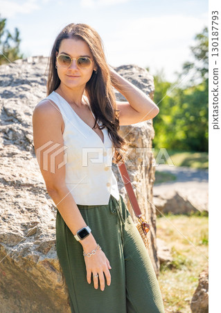 Young woman dressed in white vest and green trousers posing outdoors in Old Money style. Concept of timeless elegance, fashion confidence and classic aesthetic in modern lifestyle. Young woman dressed in white vest and green trousers posing outdoors in Old Money style. Concept of timeless elegance, fashion confidence and classic aesthetic in modern lifestyle. 130187793