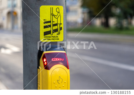 Modern yellow pedestrian crossing button on an urban pole, displaying an illuminated wait sign and clear instruction, vital for city traffic safety 130188155