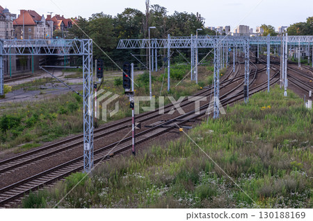 Complex railway tracks with red signals visible among lush green vegetation and urban backdrop, depicting vital city transportation infrastructure Complex railway tracks with red signals visible among lush green vegetation and urban backdrop, depicting vital city transportation infrastructure 130188169
