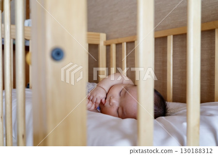 A 6-month-old baby sleeps peacefully in a wooden crib 130188312
