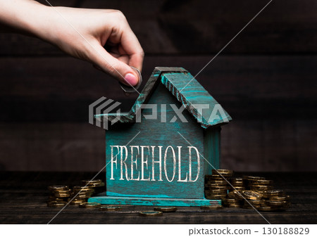 Wooden house model with coins next to it and hand 130188829