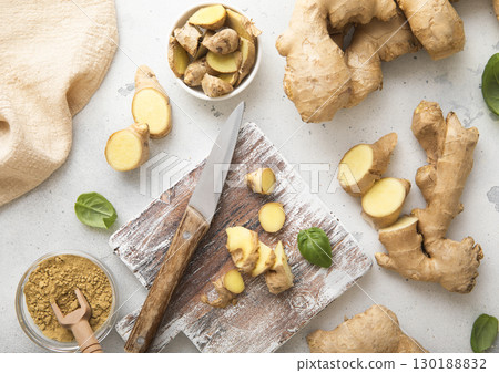 Raw fresh ginger root slices chopped with knife on wooden board with ginger powder.Top view. 130188832
