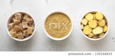 Ginger root slices and powder and ginger cubes with sugar on light kitchen background.Top view. Ginger root slices and powder and ginger cubes with sugar on light kitchen background.Top view. 130188833