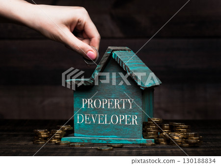 Wooden house model with coins next to it and hand 130188834