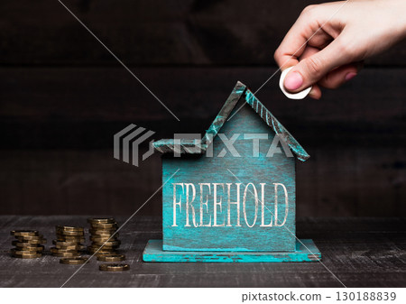 Wooden house model with coins next to it and hand 130188839