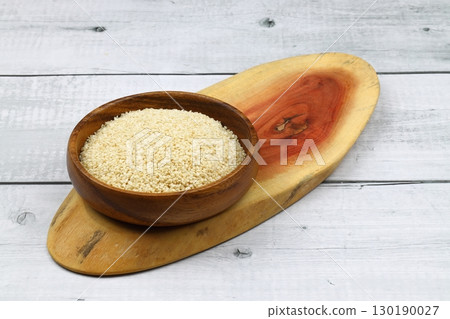 Top view closeup of freshly harvested white sesame in wooden bowl isolated on wooden background with clipping path. Top view closeup of freshly harvested white sesame in wooden bowl isolated on wooden background with clipping path. 130190027