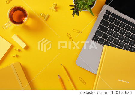 Yellow workspace with laptop, notebook, tea, plant, and stationery. Top view, space for your text. Yellow workspace with laptop, notebook, tea, plant, and stationery. Top view, space for your text. 130191686