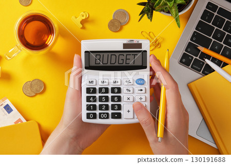 Hands holding calculator with word budget on screen. Money, laptop, and yellow stationery. Finance and business concept with copyspace. Hands holding calculator with word budget on screen. Money, laptop, and yellow stationery. Finance and business concept with copyspace. 130191688