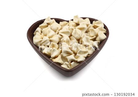 handmade manti (turkish ravioli type dumplings) on wooden heart shape bowl, before cooking. isolated on white background. 130192034