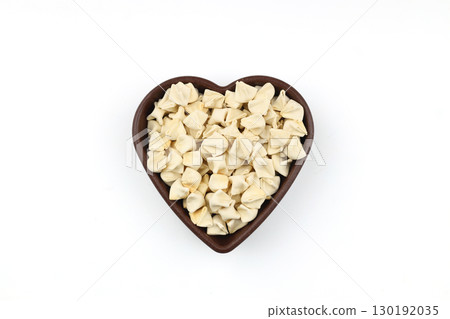 handmade manti (turkish ravioli type dumplings) on wooden heart shape bowl, before cooking. isolated on white background. 130192035