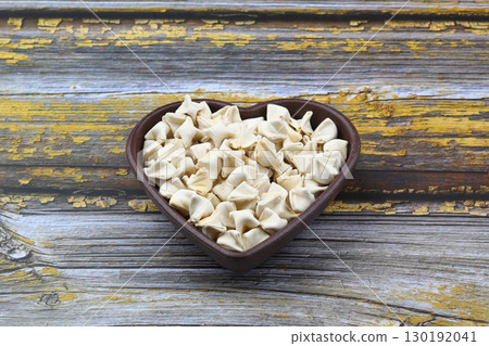 handmade manti (turkish ravioli type dumplings) on wooden heart shape bowl, before cooking 130192041