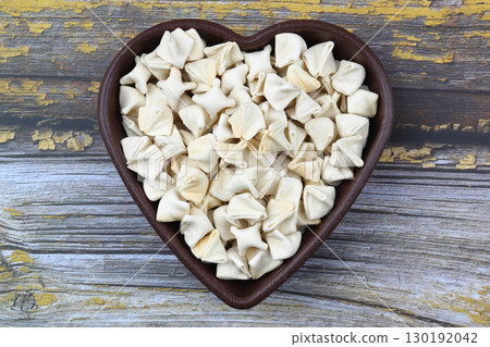 handmade manti (turkish ravioli type dumplings) on wooden heart shape bowl, before cooking 130192042