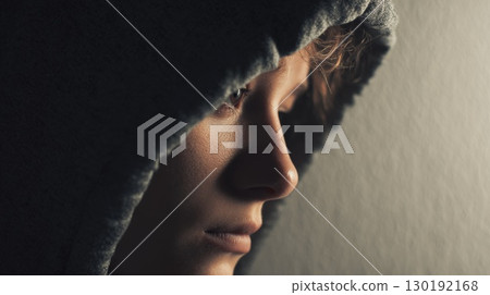 Contemplative Side Profile of a Hooded Individual in Soft Lighting 130192168