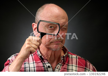 Closeup portrait of a elderly man in studio using a magnifying glass 130192246
