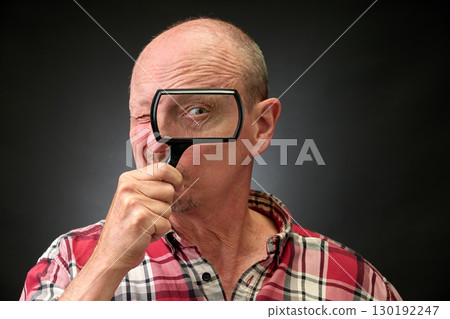 Closeup portrait of a elderly man in studio using a magnifying glass 130192247