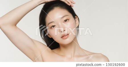 Young woman posing with arms raised showing smooth clean armpits on light background 130192600