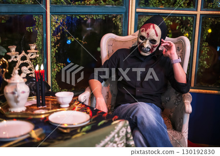 Spooky mask devil man on dinner chair and table for Halloween 2025 130192830