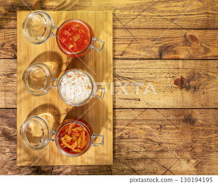 Rustic food composition with Probiotic food. Pickled or fermented vegetables. Lecho, sauerkraut, ajvar in glass jars on wooden background with copy space. Home food preserving or canning. Flat lay Rustic food composition with Probiotic food. Pickled or fermented vegetables. Lecho, sauerkraut, ajvar in glass jars on wooden background with copy space. Home food preserving or canning. Flat lay 130194195