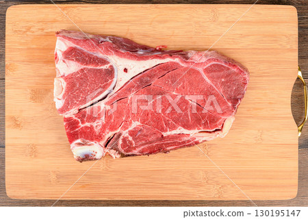 Top view of a piece of fresh beef meat on the bone on a cutting board. Top view of a piece of fresh beef meat on the bone on a cutting board. 130195147