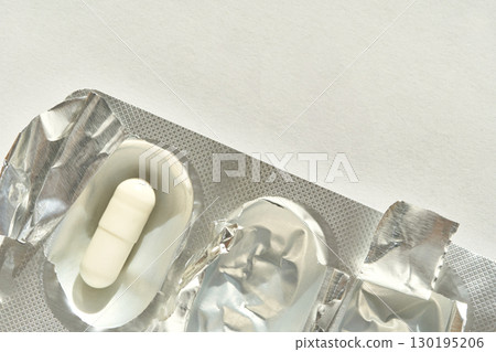 Single white pill in open blister pack with silver foil on light surface 130195206