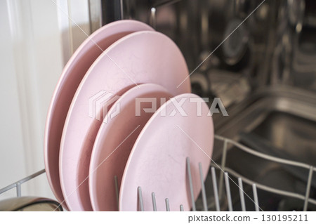 Pink plates neatly stacked in dishwasher rack in modern kitchen setting 130195211