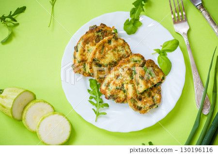fried zucchini pancakes with green onions in a plate on a green background 130196116