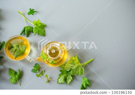 Tea in a glass teapot and cup with currant and mint leaves Tea in a glass teapot and cup with currant and mint leaves 130196130