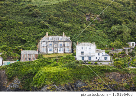 Clifftop coastal houses on lush green hillside, rugged shoreline village, scenic UK coast Clifftop coastal houses on lush green hillside, rugged shoreline village, scenic UK coast 130196403
