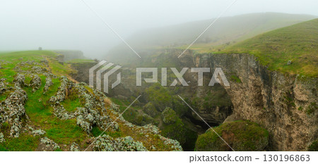 Rock formations and cracks covered with green moss in a misty landscape 130196863