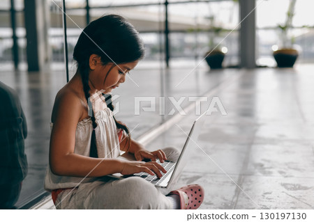 A young girl sitting on the floor, focused on her laptop, engaged in creativity and learning in a modern environment. A young girl sitting on the floor, focused on her laptop, engaged in creativity and learning in a modern environment. 130197130