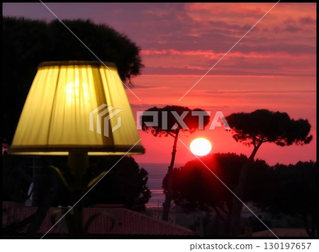 Fiery Red Sunset Over the Sea with an Illuminated Foreground Lamp 130197657