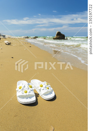 White slippers with daisy decorations resting on the sandy beach of Rodi Garganico in Apulia, Italy 130197722