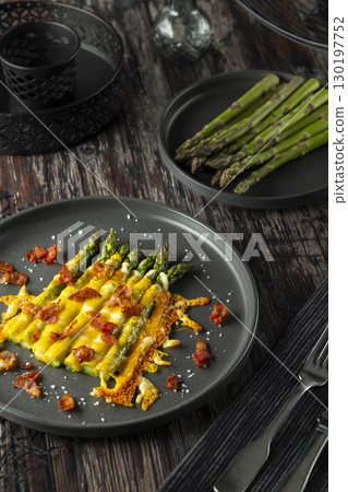 Delicious baked asparagus with melted cheese and bacon bits on a dark plate 130197752