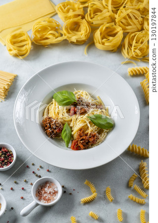 Delicious spaghetti bolognese with basil leaves and parmesan, surrounded by various types of pasta and spices Delicious spaghetti bolognese with basil leaves and parmesan, surrounded by various types of pasta and spices 130197844