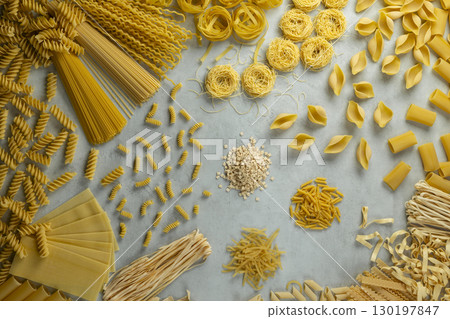 Variety of uncooked pasta shapes laying on gray background 130197847