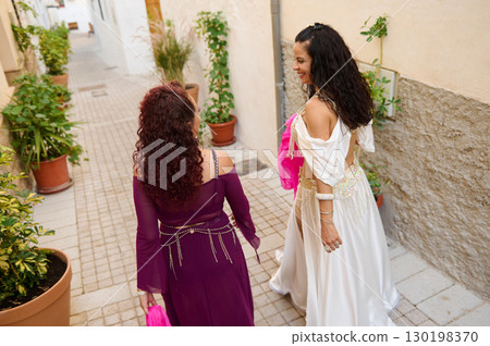 Two Women Enjoying a Charming Alleyway in Colorful Dresses and Smiles 130198370