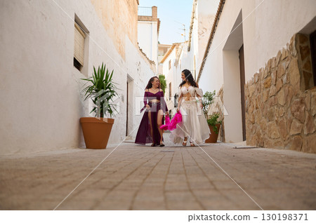 Two Women in Vibrant Costumes Strolling in a Quaint Mediterranean Alley 130198371