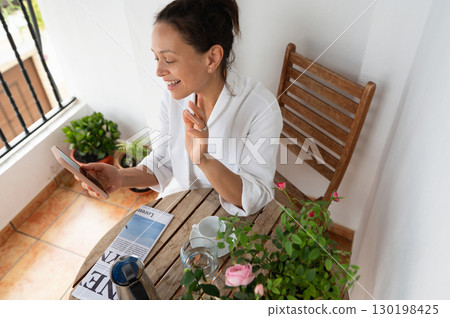 Woman Enjoying a Relaxing Video Call on a Cozy Balconry 130198425