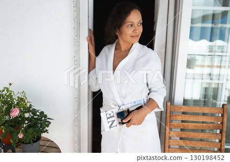 Woman Relaxing at Home in White Robe Holding Magazines and Smartphone Woman Relaxing at Home in White Robe Holding Magazines and Smartphone 130198452