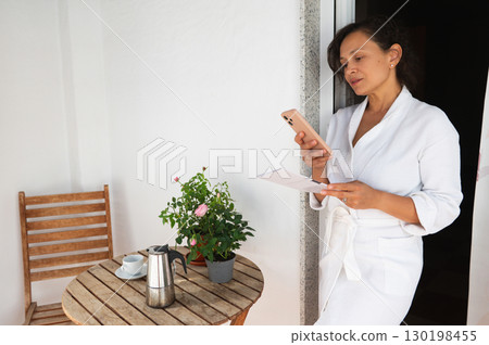 Woman Relaxing With Coffee and Phone on a Patio in Morning Light Woman Relaxing With Coffee and Phone on a Patio in Morning Light 130198455