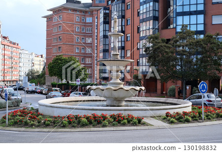 A beautiful multi-tiered fountain stands as the centerpiece of a roundabout in a modern European city 130198832