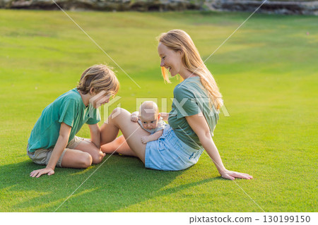 Mother, older son, and newborn baby on a meadow in the park. Family spending quality time together in nature. Parenthood, love, and family bond concept Mother, older son, and newborn baby on a meadow in the park. Family spending quality time together in nature. Parenthood, love, and family bond concept 130199150